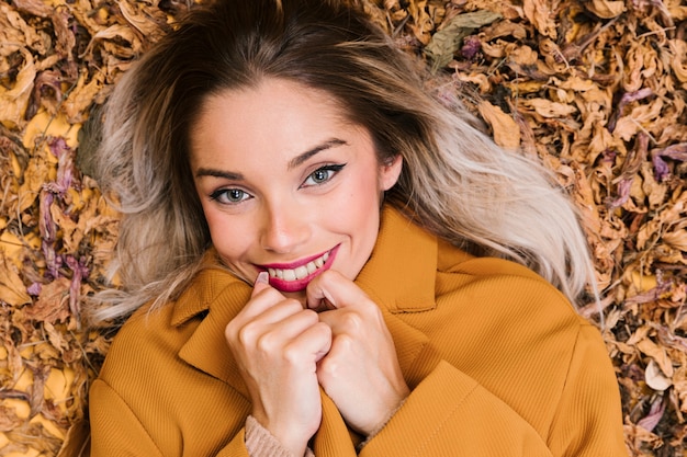 Free photo smiling modern woman lying on dry leaves holding yellow jacket looking at camera