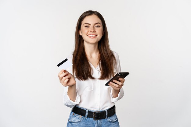 신용 카드와 휴대 전화를 사용하여 웃고 있는 현대 여성이 sm에서 온라인 쇼핑을 하고 있습니다.