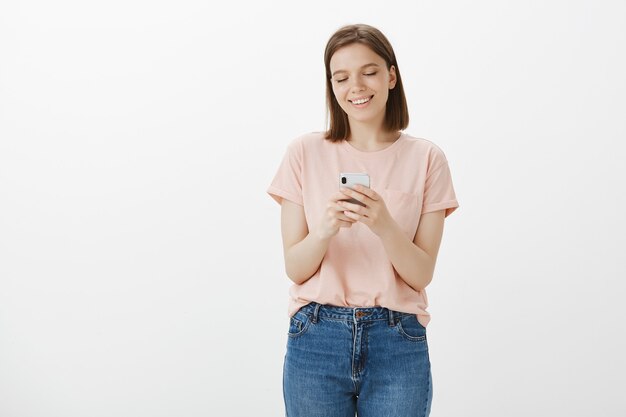 Улыбающаяся современная женщина с помощью мобильного телефона, текстовых сообщений в социальной сети