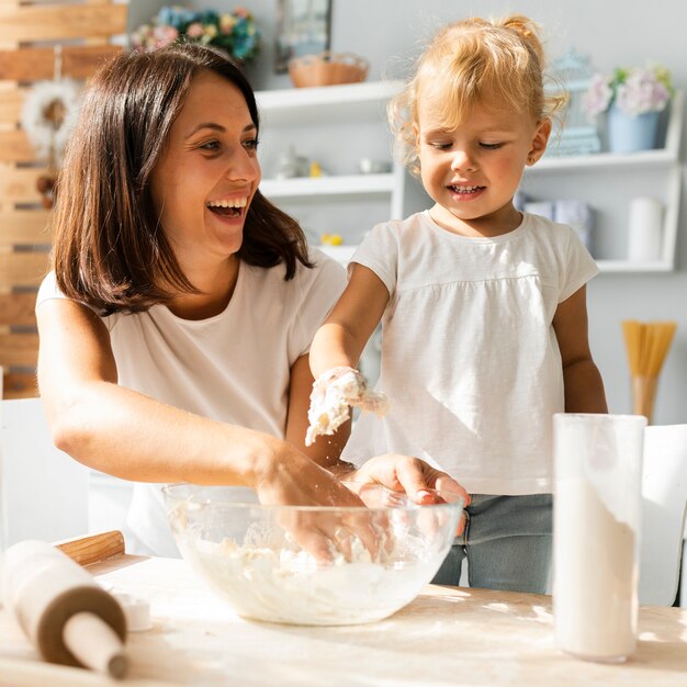 Smiling mother and cute daughter preparing dough