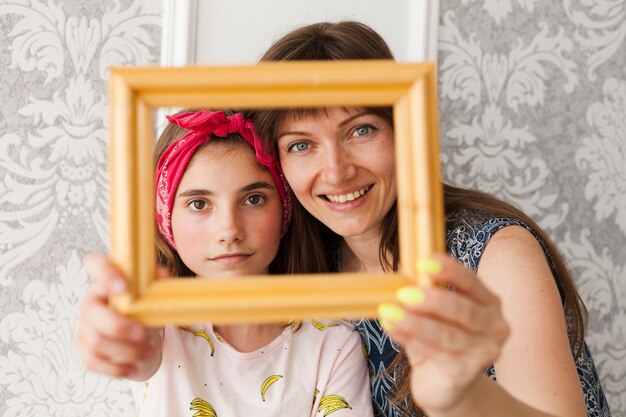 Smiling mother and daughter holding photo frame in front of their face