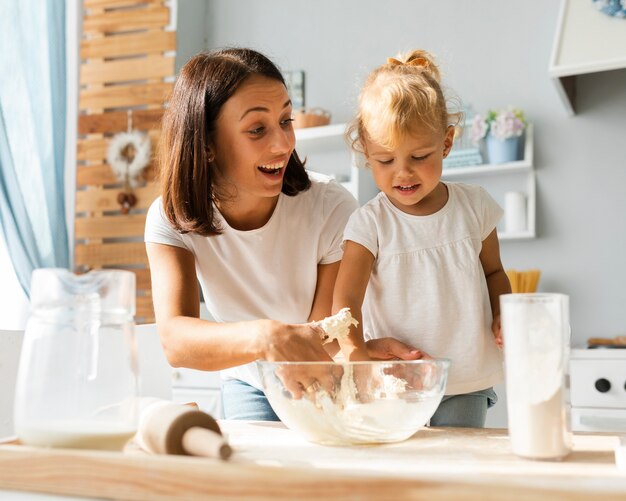 Smiling mother and daughter preparing dough