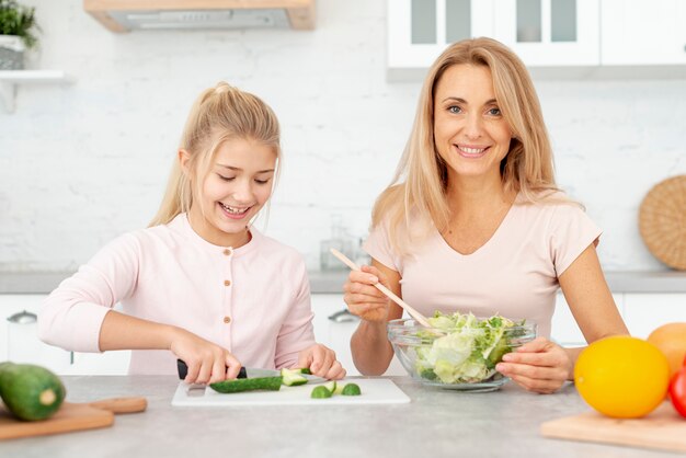 Улыбаясь, мать и дочь готовят салат