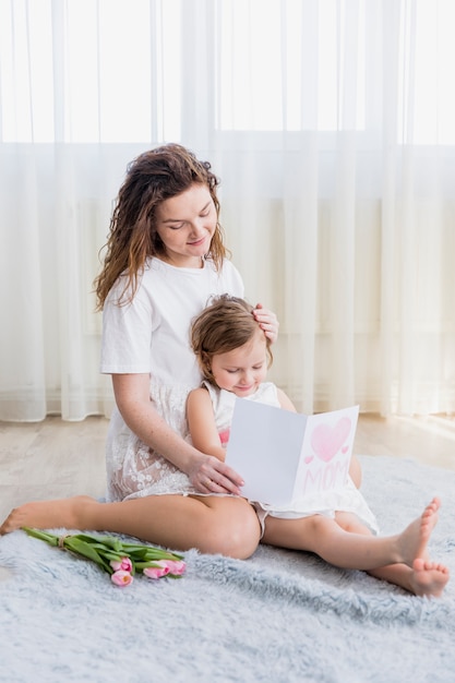Smiling mother and daughter reading greeting card at home