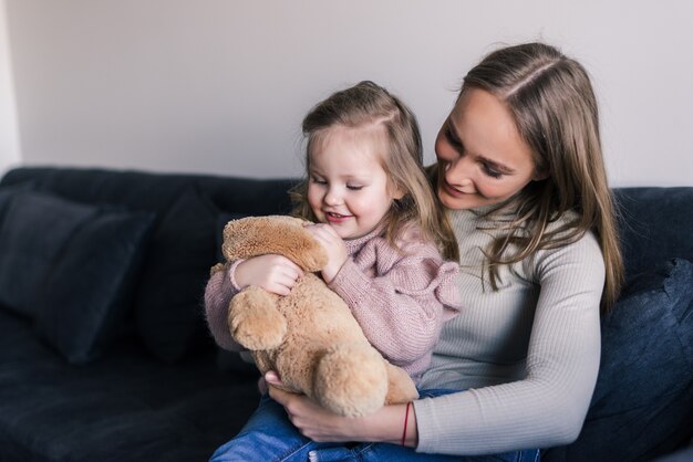 Smiling mother hugging cute little girl holding teddy bear toy showing love and care in family