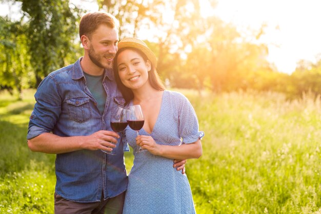 Smiling multiethnic couple embracing with glasses in park