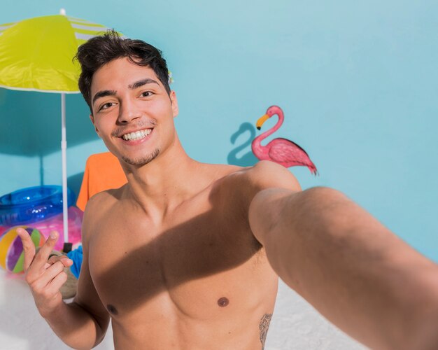 Smiling muscular guy on beach taking selfie