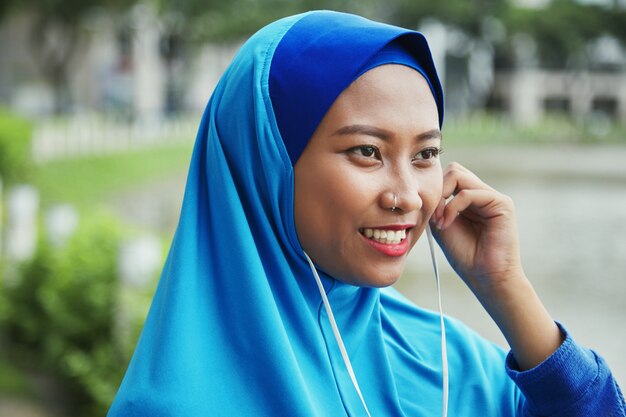 Smiling Muslim woman plugging earphones on street