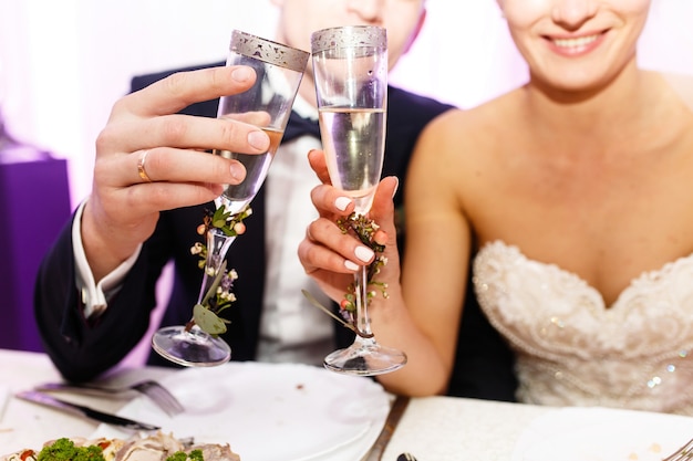 Smiling newlyweds clang their glasses sitting at the table 