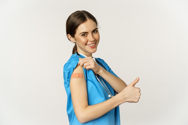 Smiling nurse medical worker showing thumbs up and shoulder after vaccine covid vaccination campaign...