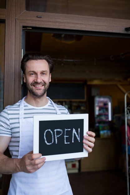 Smiling owner holding a open sign at bakery shop entrance