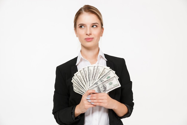 Smiling pensive blonde business woman holding money and looking away over white wall