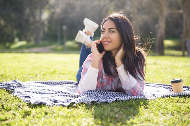 Smiling pensive girl resting on grass and speaking on cell