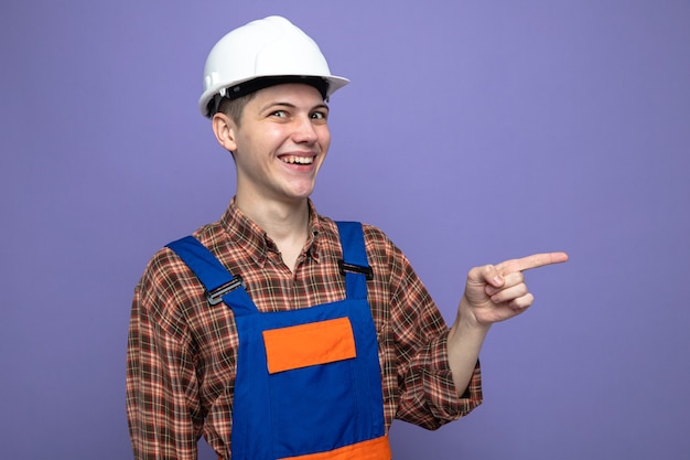 Smiling points at side young male builder wearing uniform 