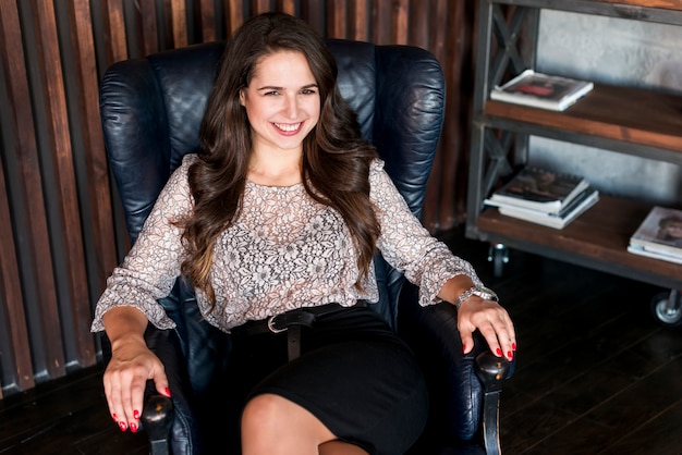 Free photo smiling portrait of an attractive young woman sitting on armchair