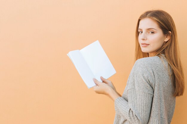 Smiling portrait of a beautiful young woman holding book in hand looking at camera