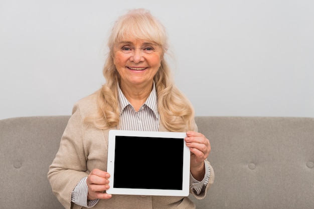 Smiling portrait of blonde senior woman showing digital tablet with blank screen