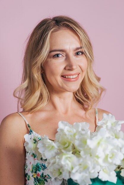Smiling portrait of blonde young woman holding white fresh flowers against colored background