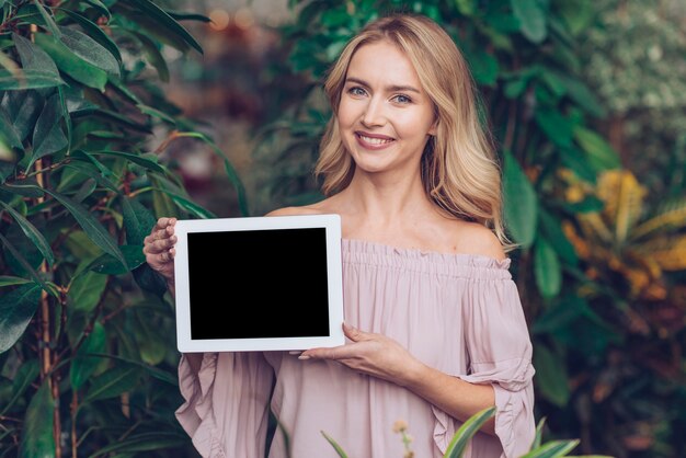 Smiling portrait of a blonde young woman showing blank display digital tablet