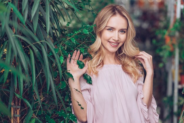 Smiling portrait of a blonde young woman standing near the green plants