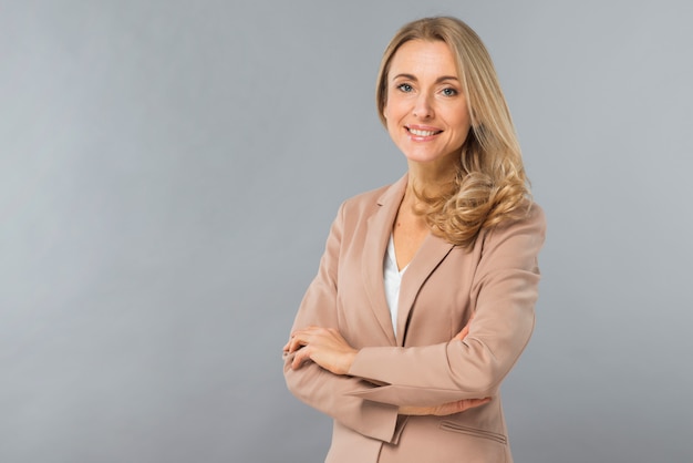 Smiling portrait of a confident blonde young woman standing against gray backdrop