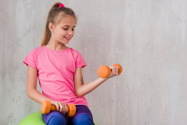 Free photo smiling portrait of a girl exercising with dumbbell against wall