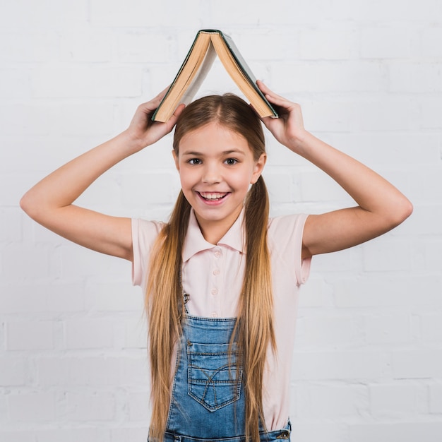 Ritratto sorridente di una ragazza che tiene un libro aperto sulla sua testa che guarda alla macchina fotografica