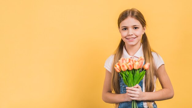 Улыбающийся портрет девушки с оранжевыми тюльпанами в руках на желтом фоне