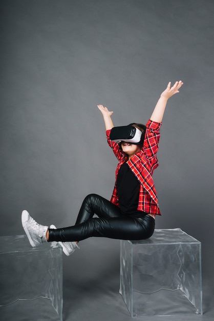 Free photo smiling portrait of a girl sitting on blocks raising her arms against gray background