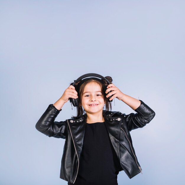 Smiling portrait of a girl wearing black jacket listening music on headphone