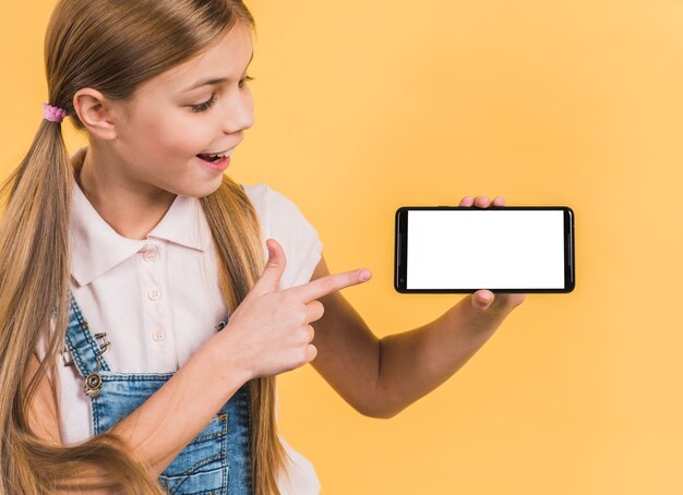 Smiling portrait of a girl with long blonde hair pointing at mobile phone showing white blank screen