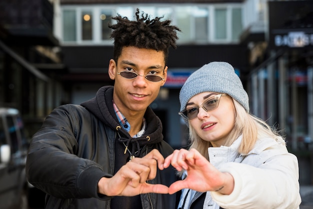 Smiling portrait of interracial couple wearing sunglasses making heart shape with their hands