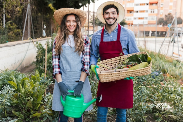 Smiling portrait of a male and female gardener holding watering can and basket in the garden