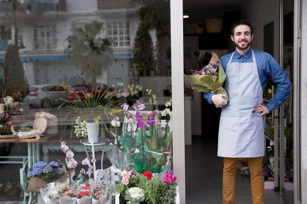 Smiling portrait of a male holding flower bouquet standing at the entrance of florist shop
