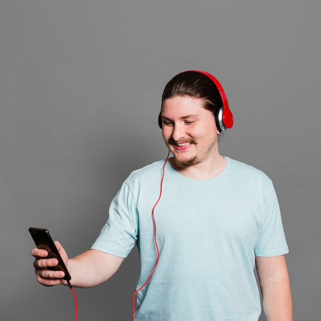 Smiling portrait of a man listening music on headphone through mobile phone against grey wall