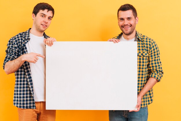 Smiling portrait of a man showing white blank placard against yellow backdrop