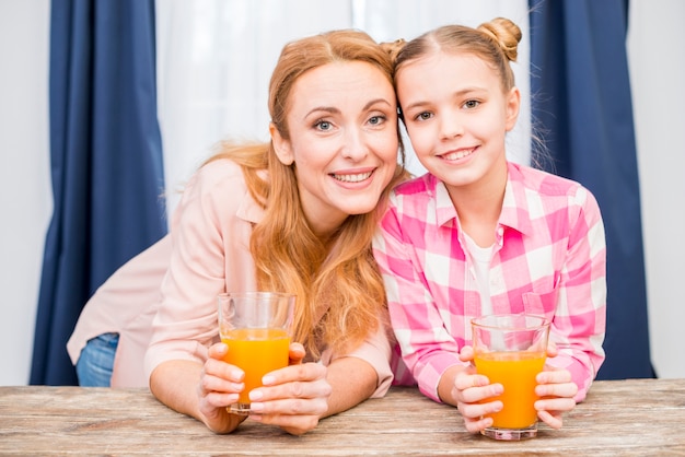 Smiling portrait of a mother and her daughter holding glass of juice