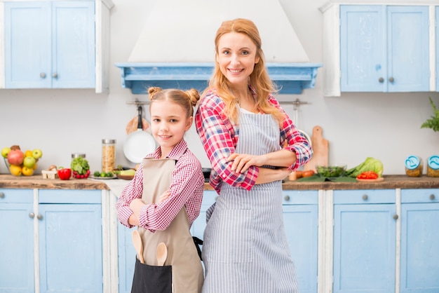 Smiling portrait of a mother and her daughter standing back to back with their arms crossed