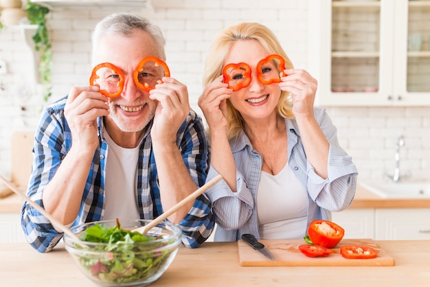 Ritratto sorridente di una coppia senior che guarda attraverso la fetta rossa del peperone dolce