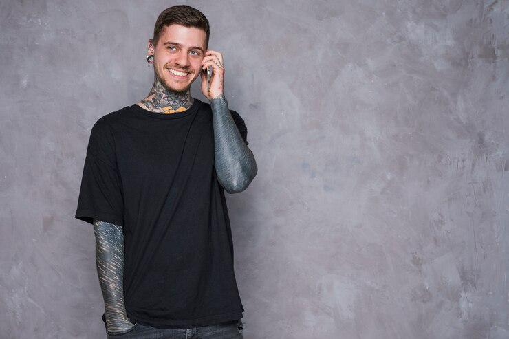 Free Photo smiling portrait of a tattooed young man with pierced ears talking on mobile phone