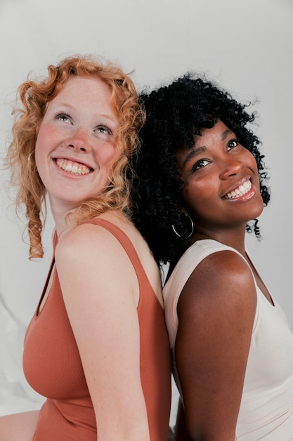 Smiling portrait of a young african and caucasian women sitting back to back looking up