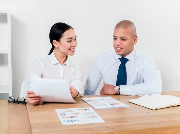 Free photo smiling portrait of a young businessman and businesswoman discussing the report at workplace