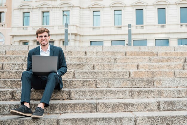 デジタルタブレットを使用して階段の上に座っている青年実業家の肖像画を笑顔