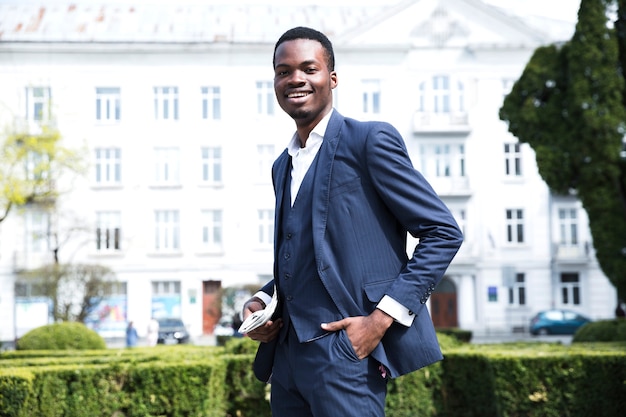 Free photo smiling portrait of a young businessman with hands in his pocket looking at camera