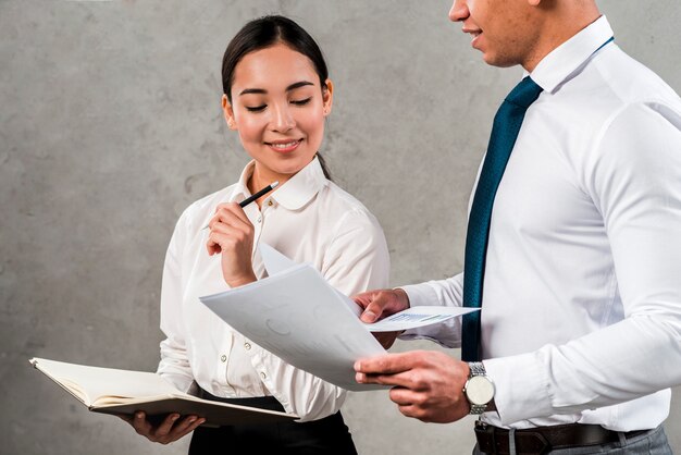 彼女の同僚によって保持されているドキュメントを見て手で日記を保持している若い実業家の肖像画を笑顔