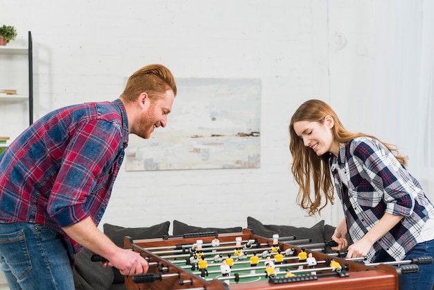 Smiling portrait of a young couple enjoying playing the table soccer game in the living room