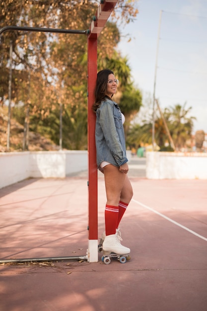 Усмехаясь портрет молодой женщины конькобежца стоя около цели футбола