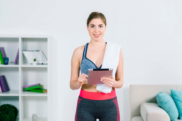 Smiling portrait of a young fit woman touching digital tablet at home