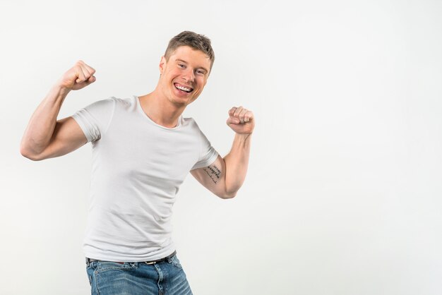 Smiling portrait of a young man flexing her muscles against white background