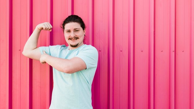 Smiling portrait of young man flexing his muscle against red corrugated wall